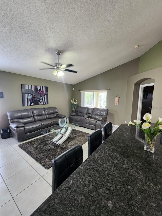 living room with lofted ceiling, a textured ceiling, ceiling fan, and light tile patterned floors