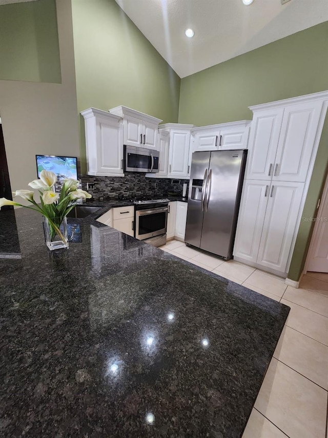 kitchen with stainless steel appliances, dark stone counters, light tile patterned floors, white cabinets, and high vaulted ceiling