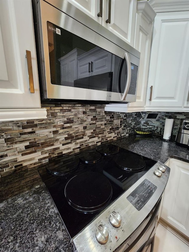 room details featuring appliances with stainless steel finishes, decorative backsplash, white cabinetry, and dark stone counters