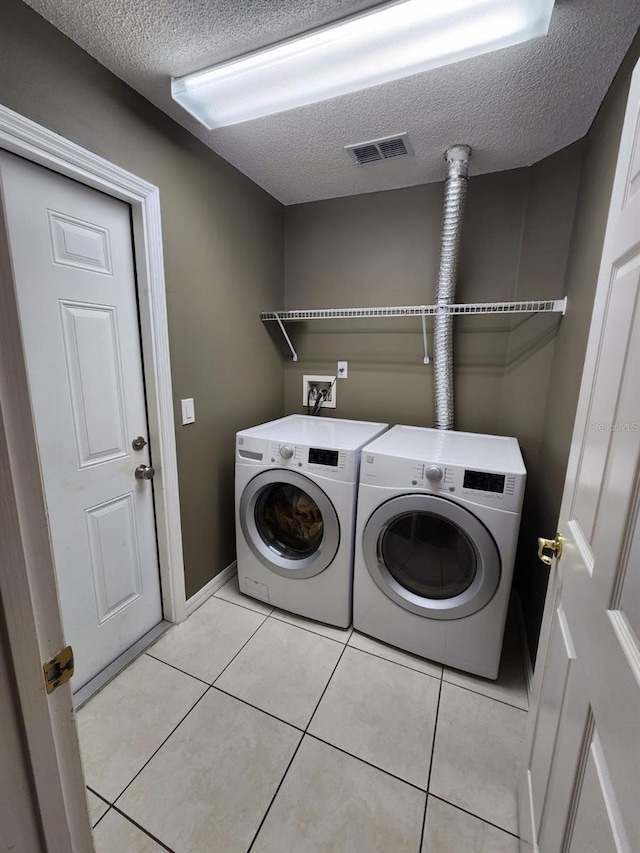 washroom featuring a textured ceiling, washer and clothes dryer, and light tile patterned floors