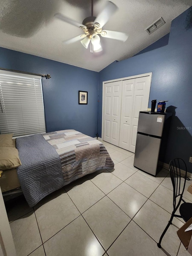 tiled bedroom with lofted ceiling, ceiling fan, a textured ceiling, stainless steel refrigerator, and a closet