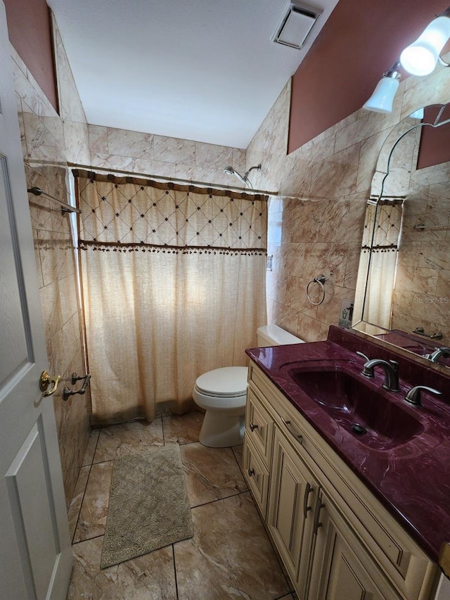 bathroom with toilet, vanity, a tile shower, and tile walls