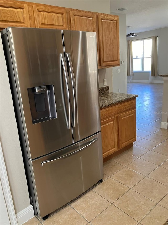 kitchen featuring stainless steel fridge, light tile floors, and dark stone countertops