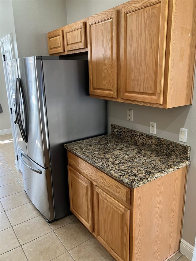 kitchen with dark stone countertops, stainless steel refrigerator, and light tile floors