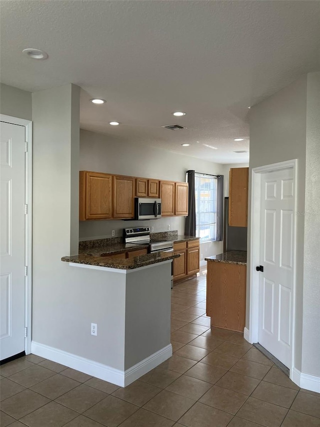 kitchen with tile floors, stainless steel appliances, kitchen peninsula, and dark stone countertops