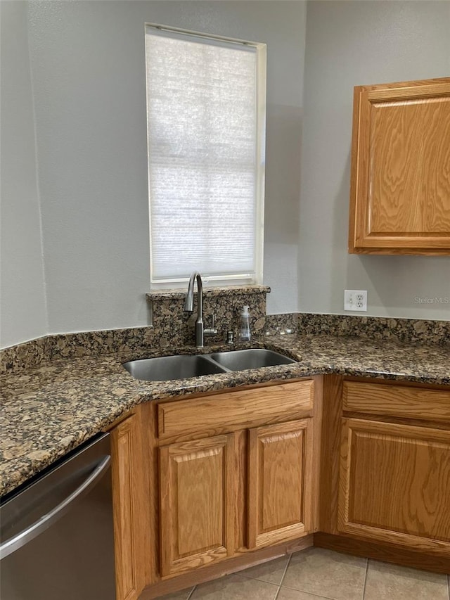 kitchen with sink, dishwasher, light tile flooring, and dark stone countertops