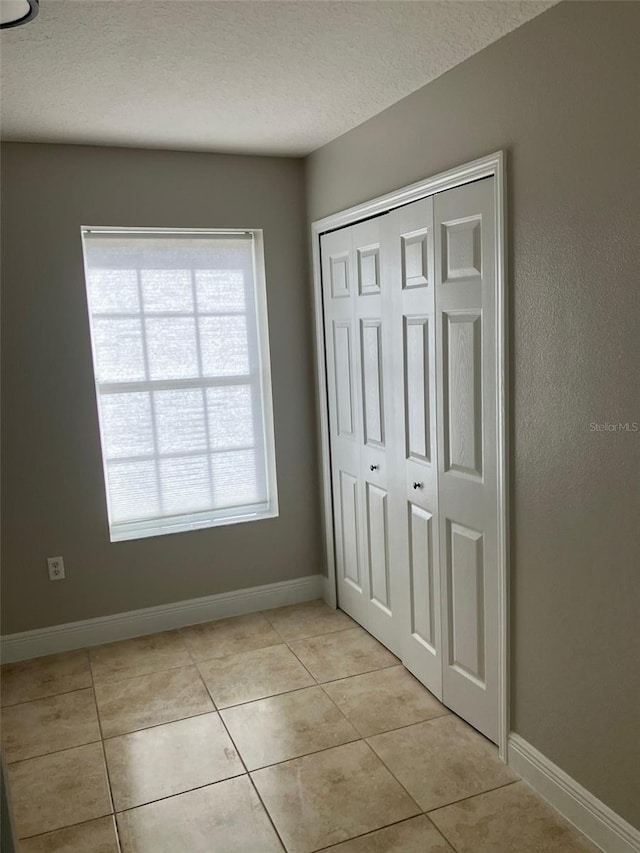 unfurnished bedroom with a closet, light tile flooring, and multiple windows