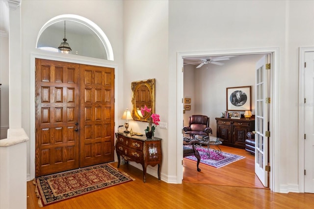 foyer featuring french doors, a towering ceiling, wood-type flooring, and ceiling fan