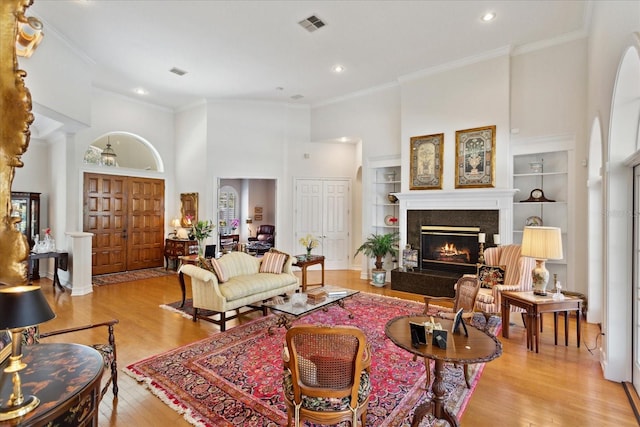 living room featuring light hardwood / wood-style floors, a high end fireplace, a high ceiling, and built in shelves