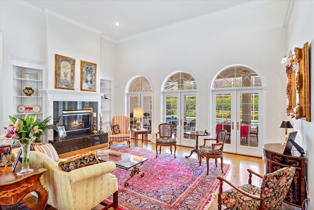 living room featuring a premium fireplace, hardwood / wood-style flooring, ornamental molding, a towering ceiling, and french doors