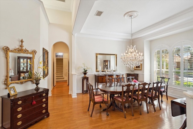 dining space with an inviting chandelier, ornamental molding, light wood-type flooring, and a raised ceiling