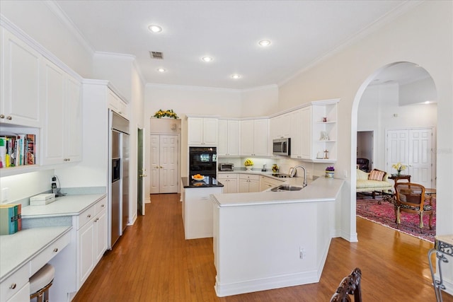 kitchen with appliances with stainless steel finishes, sink, light wood-type flooring, kitchen peninsula, and white cabinetry