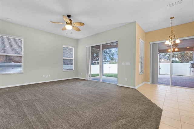 carpeted spare room featuring ceiling fan with notable chandelier