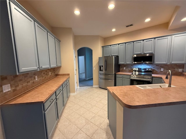 kitchen with appliances with stainless steel finishes, gray cabinets, kitchen peninsula, and sink