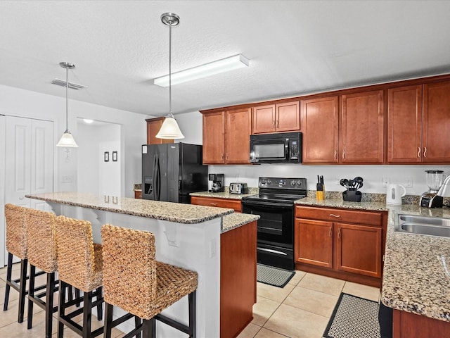 kitchen featuring decorative light fixtures, black appliances, a kitchen island, light tile floors, and a breakfast bar