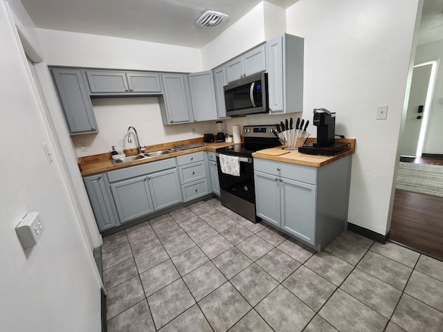 kitchen with stainless steel appliances, sink, wood counters, and light tile flooring