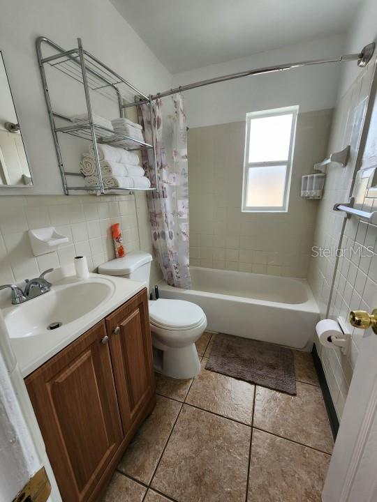 full bathroom featuring tile walls, toilet, tasteful backsplash, shower / bath combination with curtain, and vanity