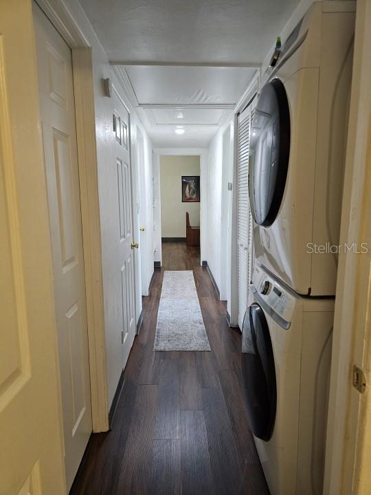 laundry room featuring stacked washer / drying machine and dark hardwood / wood-style flooring