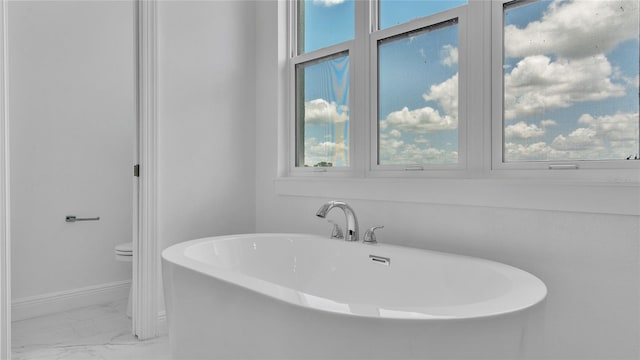 bathroom with toilet, a washtub, a wealth of natural light, and tile patterned flooring