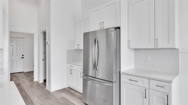 kitchen featuring white cabinets, stainless steel fridge, light hardwood / wood-style floors, backsplash, and light stone countertops