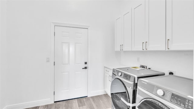 clothes washing area featuring separate washer and dryer, light hardwood / wood-style flooring, and cabinets