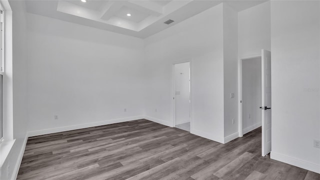 spare room featuring dark wood-type flooring, beamed ceiling, coffered ceiling, and a high ceiling