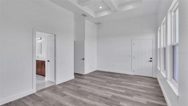 spare room featuring a healthy amount of sunlight, beam ceiling, light wood-type flooring, and a towering ceiling