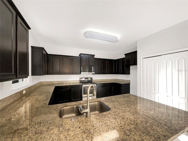 kitchen featuring dark brown cabinetry, stainless steel appliances, light stone counters, and sink