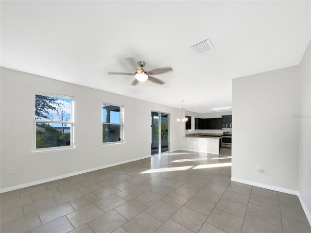 tiled empty room with ceiling fan with notable chandelier