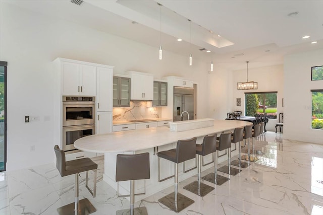 kitchen featuring tasteful backsplash, a large island with sink, a kitchen bar, appliances with stainless steel finishes, and light tile floors