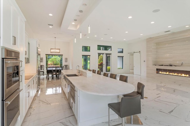 kitchen featuring double oven, white cabinets, light tile flooring, a center island with sink, and sink