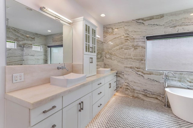 bathroom featuring a bath to relax in, double sink vanity, tile walls, and tile floors