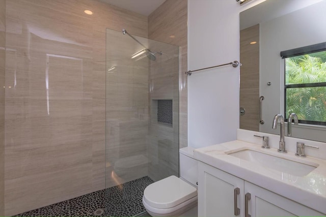 bathroom with tiled shower, vanity, and toilet