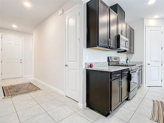 kitchen with stainless steel appliances, light stone counters, dark brown cabinets, and light tile floors