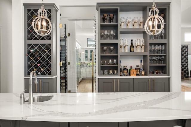 bar with pendant lighting, light hardwood / wood-style floors, light stone counters, and sink