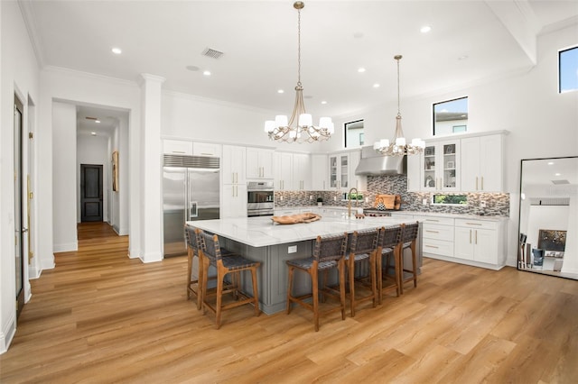 kitchen with white cabinets, a kitchen breakfast bar, a spacious island, built in refrigerator, and light hardwood / wood-style floors