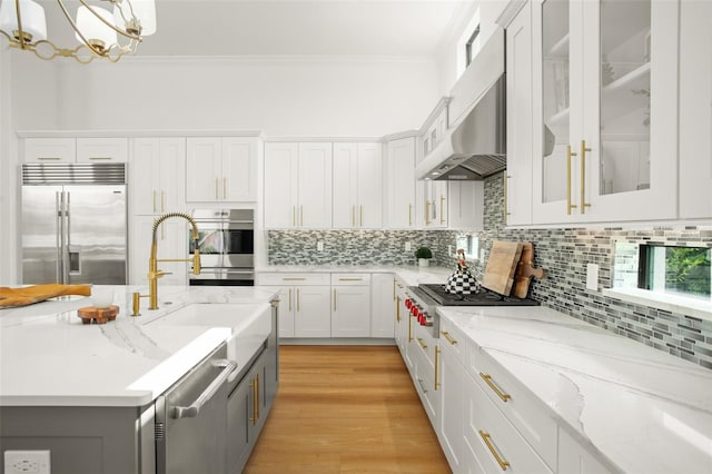 kitchen with hanging light fixtures, appliances with stainless steel finishes, light hardwood / wood-style floors, light stone counters, and white cabinetry