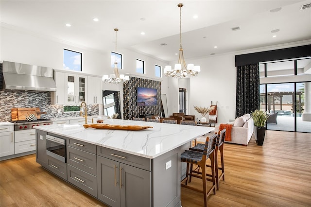 kitchen with white cabinetry, a center island with sink, stainless steel appliances, and wall chimney range hood