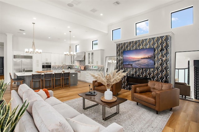 living room featuring a chandelier, a high ceiling, light wood-type flooring, and crown molding