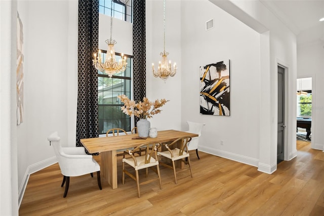 dining room with wood-type flooring, a towering ceiling, and ornamental molding