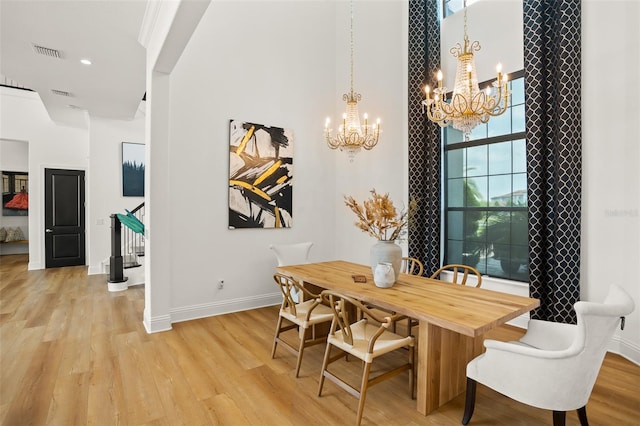 dining room with light wood-type flooring, a towering ceiling, and an inviting chandelier