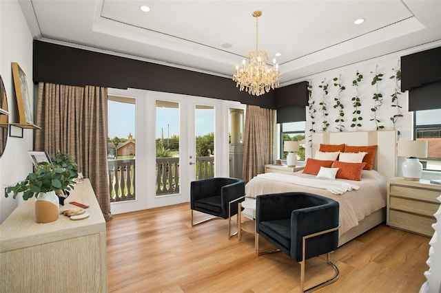 bedroom with access to exterior, light wood-type flooring, a tray ceiling, and an inviting chandelier