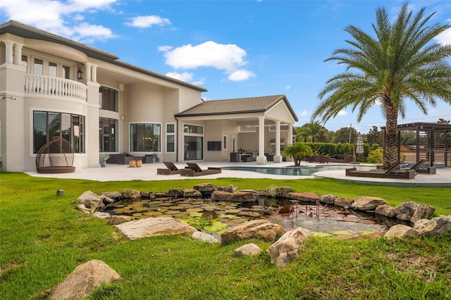 rear view of property with a lawn, a balcony, and a patio