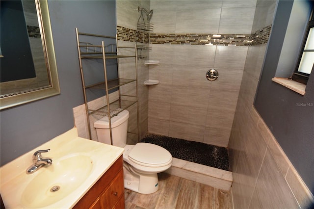 bathroom featuring a tile shower, hardwood / wood-style flooring, toilet, tile walls, and oversized vanity