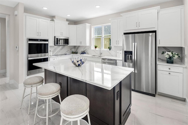 kitchen with white cabinetry, light stone countertops, a kitchen island, appliances with stainless steel finishes, and tasteful backsplash