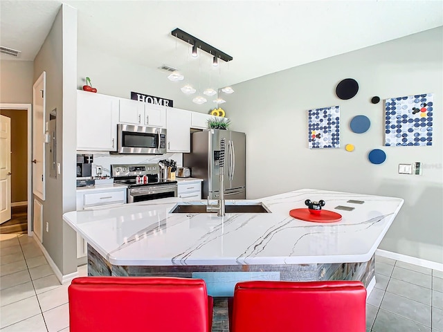 kitchen with stainless steel appliances, white cabinets, an island with sink, track lighting, and light tile patterned floors