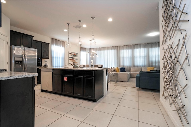 kitchen featuring hanging light fixtures, stainless steel appliances, a kitchen island with sink, and light tile floors