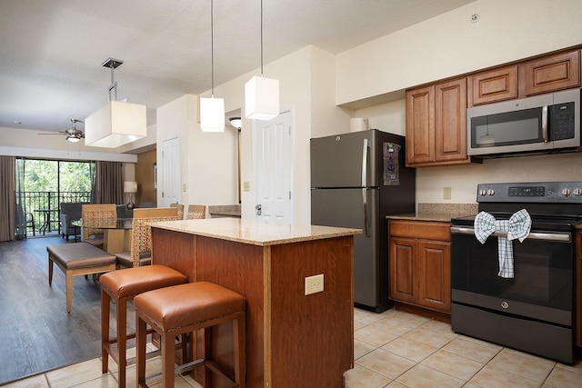 kitchen featuring ceiling fan, a center island, stainless steel appliances, light stone counters, and light tile patterned floors