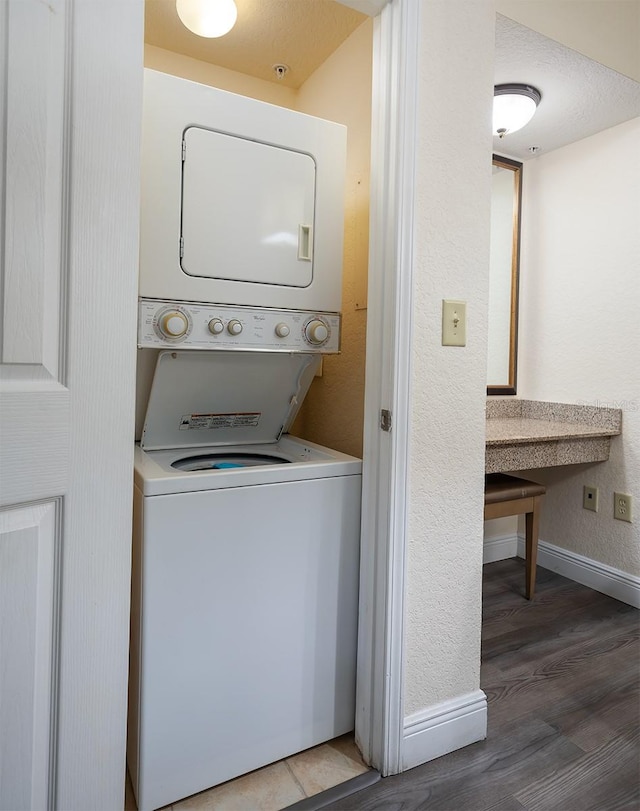 clothes washing area featuring a textured ceiling, stacked washer / dryer, and dark wood-type flooring