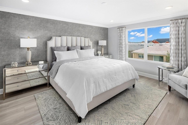 bedroom featuring an accent wall, wood finished floors, baseboards, ornamental molding, and wallpapered walls